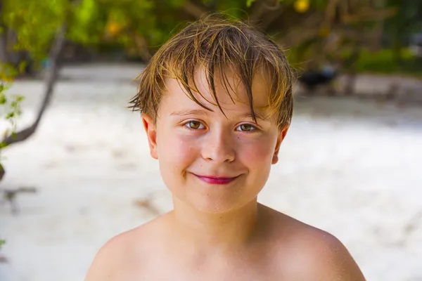 Niño feliz con el pelo mojado en la playa sonríe y se ve muy seguro de sí mismo —  Fotos de Stock