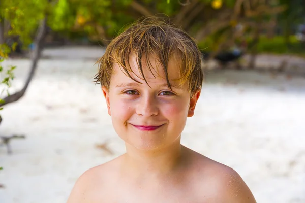 Niño feliz con el pelo mojado en la playa sonríe y se ve muy seguro de sí mismo —  Fotos de Stock
