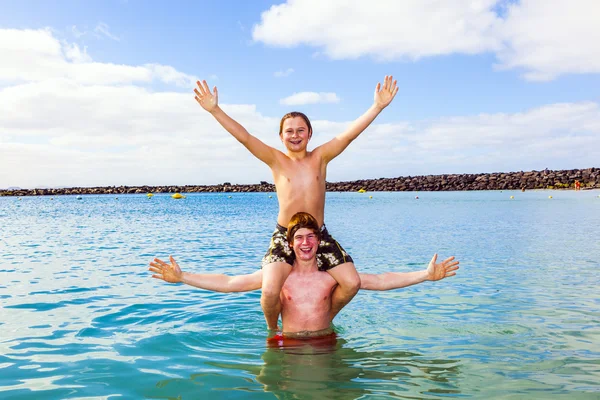 Chicos divertirse jugando piggy-back en el océano —  Fotos de Stock