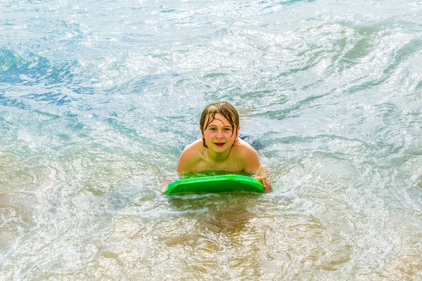 Pojken har kul med surfbräda på stranden — Stockfoto