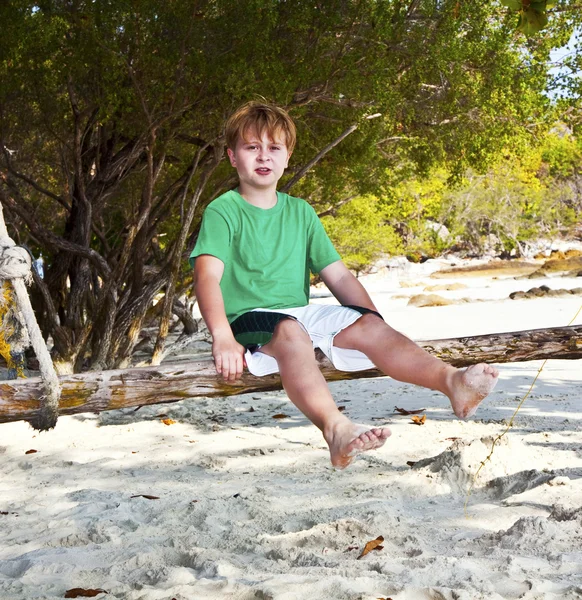 Niño sentado en un columpio en la playa bajo los árboles —  Fotos de Stock