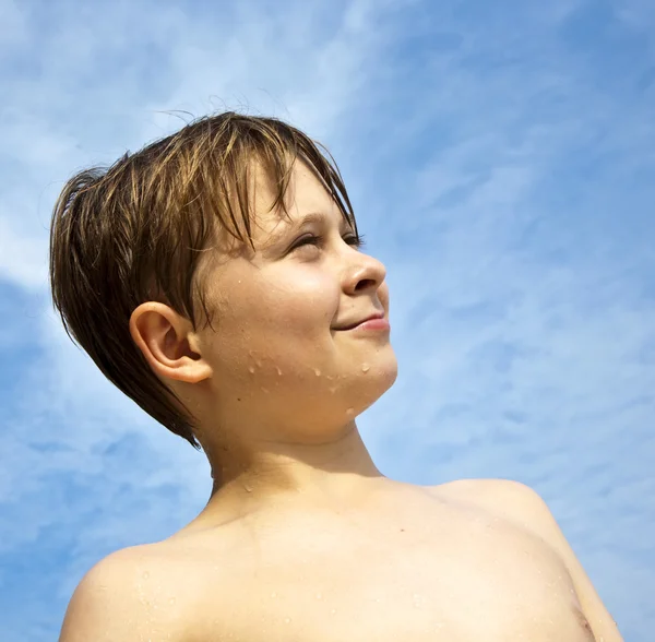 Glad ung pojke med brunt hår och ögon på stranden ler — Stockfoto