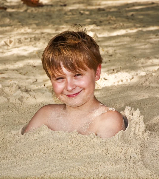 Menino feliz coberto por areia fina na praia — Fotografia de Stock