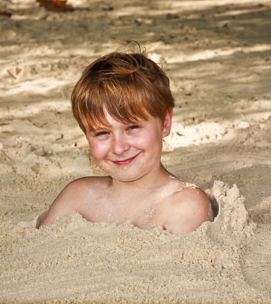 Niño feliz cubierto de arena fina en la playa —  Fotos de Stock