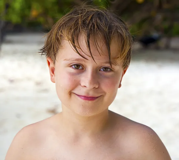 Niño feliz con el pelo mojado en la playa sonríe y se ve muy auto — Foto de Stock