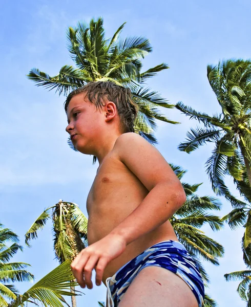 Menino andando na praia com coqueiros no céu — Fotografia de Stock