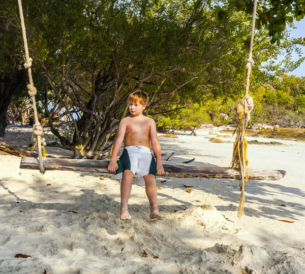 Niño sentado en un columpio en la playa bajo los árboles —  Fotos de Stock