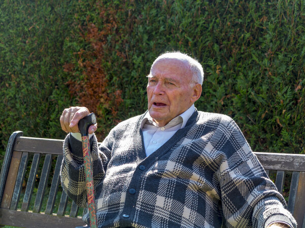 Old man enjoys sitting on a bench in his garden
