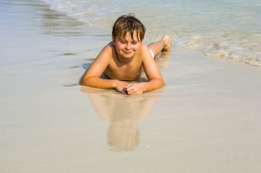 Çocuk sahilde yatan ve su ve kendini arıyor hoşlanıyor