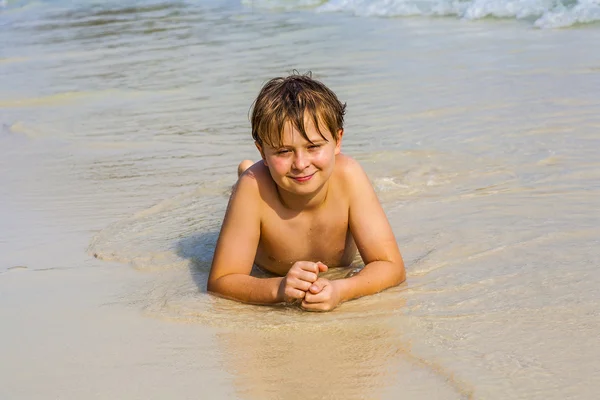 Ragazzo è sdraiato in spiaggia e gode l'acqua e guardando sé — Foto Stock