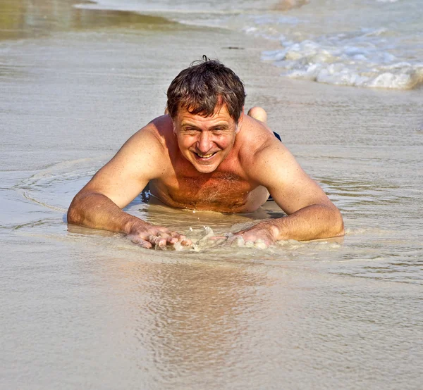 Homem de fato de banho está deitado na praia e desfrutando da saltwa — Fotografia de Stock