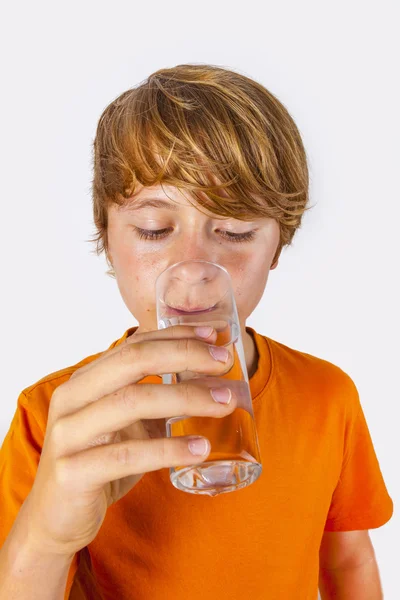 Schattige jongen met oranje shirt water drinkt Stockfoto