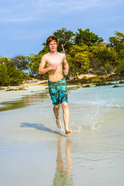Fiatal fiú jogging a trópusi tengerpart mentén piros hajjal — Stock Fotó