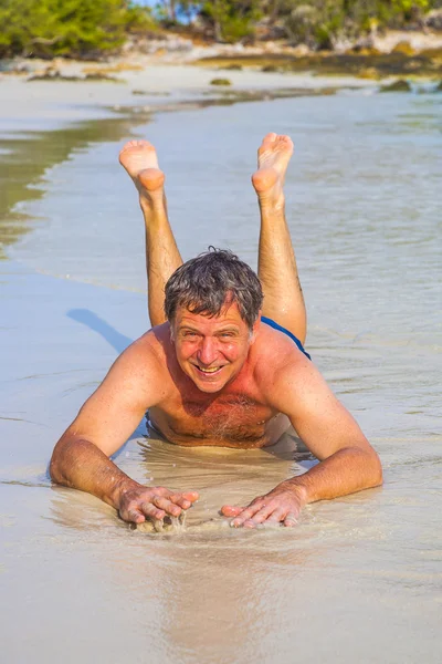 Man in badpak is liggend op het strand en genieten van de zout water met kleine golven en glimlacht — Stockfoto