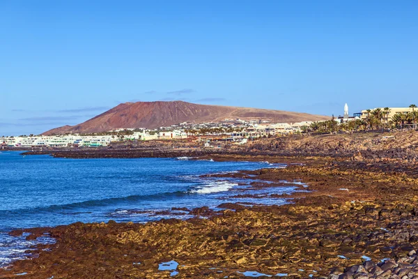 Strand en dorpje van playa blanca met de vulkaan montana roja — Stockfoto