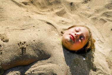 young girl is covered by sand at the beach clipart