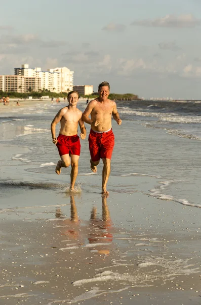 Far och son njuta jogga längs stranden — Stockfoto