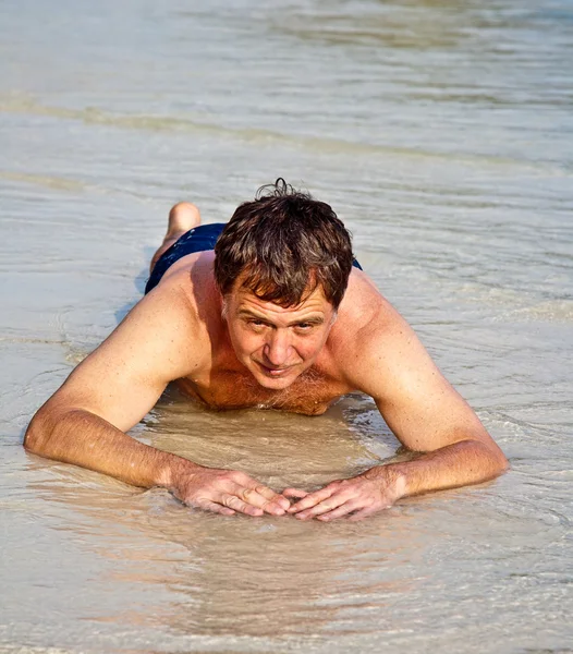 Hombre en traje de baño está tumbado en la playa y disfrutando de la saltwa — Foto de Stock