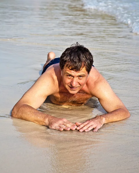 Mannen i bathingsuit ligger på stranden och njuter av saltwa — Stockfoto