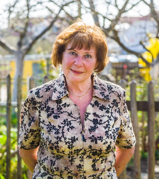 Elderly woman is standing proud in her garden and smiles — Stock Photo, Image