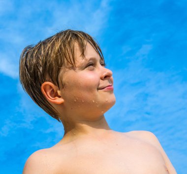 Arka planda mavi gökyüzü olan mutlu gülümseyen genç çocuk.