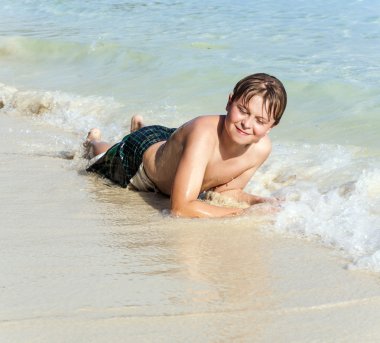Çocuk sahilde yatıyor ve kuma haddeleme sahiptir