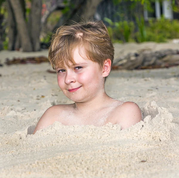 Menino coberto por areia fina na praia — Fotografia de Stock