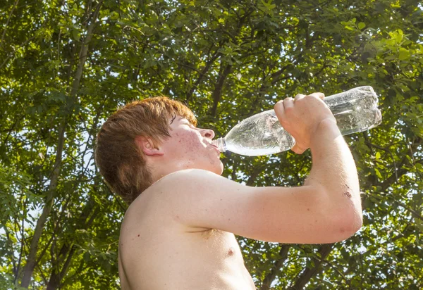 Giovane ragazzo beve acqua da una bottiglia nel calore — Foto Stock