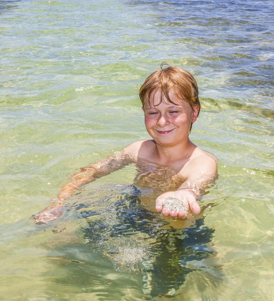 Chico en el océano muestra arena limpia en su mano —  Fotos de Stock