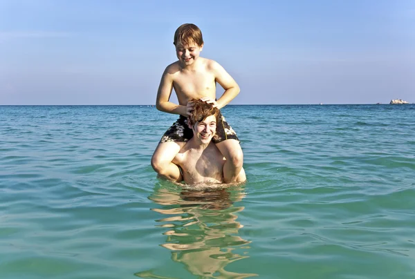 Brothers enjoy the clear warm water and playpickaback — Stock Photo, Image