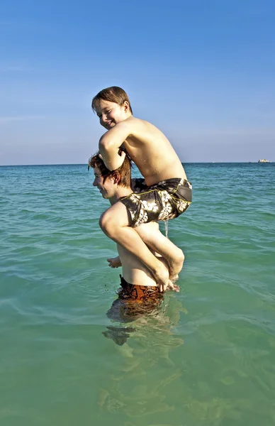 Hermanos disfrutan del agua tibia clara y playpickaback —  Fotos de Stock