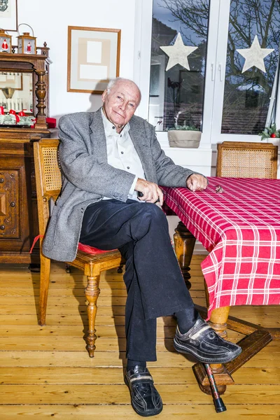 Старый дедушка сидит со своей тростью за столом — стоковое фото