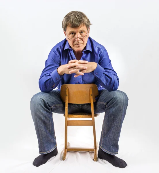 Muž sedí na malé dřevěné židle a představuje — Stock fotografie