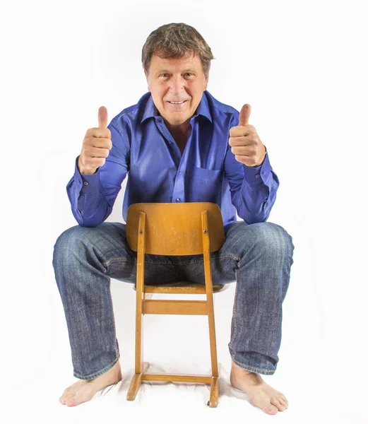 Мужчина сидит на маленьком деревянном стуле и показывает большими пальцами вверх табличку — стоковое фото
