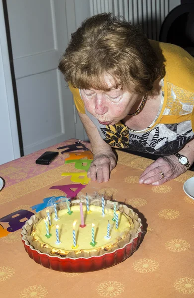 Senior female blows out candles on a cake — Stock Photo, Image