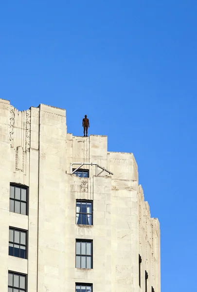 En jernstatue av mennesket fra kunstneren Antonius Gormley på taket av en m – stockfoto