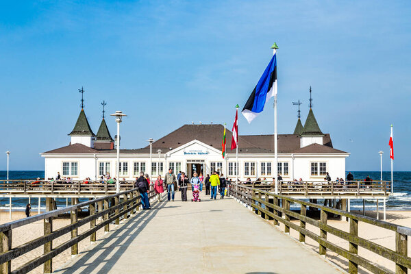 Ahlbeck, Germany - April 20, 2014: people enjoy pier and beach of Heringsdorf, Germany. The baltic Sea in Usedom Island is famous for its unique roofed wicker beach chairs.