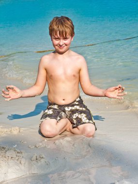 Çocuk kumsalda oynuyor ve elleriyle işaret veriyor.