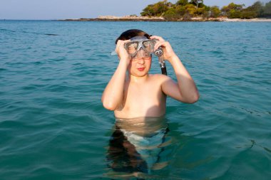 Genç çocuk güzel, berrak denizde suyun tadını çıkarıyor ve şnorkelle yüzmeye başlıyor.