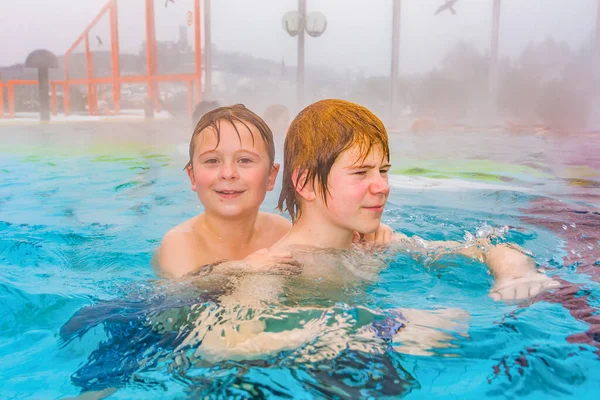 兄弟は暖かい水の中のウィンタータイムの熱プールの外のエリアで泳いでいます霧です — ストック写真