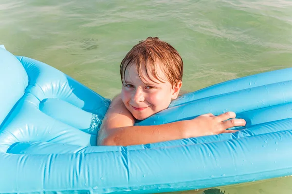 笑着的男孩喜欢在清澈的水中带着气垫漂浮 — 图库照片
