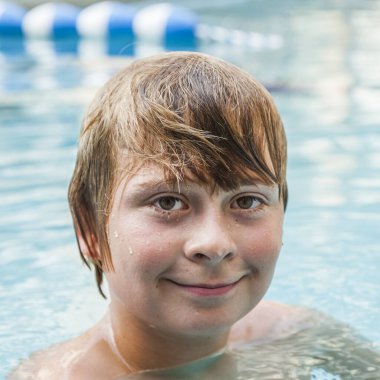 Yakışıklı çocuk açık havuzda yüzmeyi seviyor.