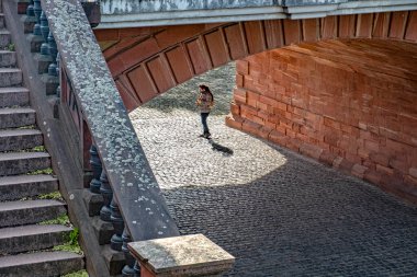 Frankfurt, Almanya - 10 Nisan 2022: köprünün altında saksafon çalan ve kumtaşı köprüsünün akustik tadını çıkaran adam.