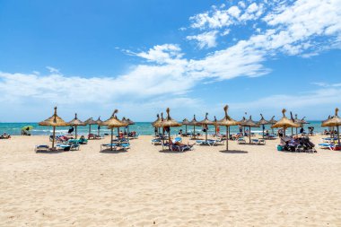 palma, Spain - June 22, 2022: people rent a beach couch unter a wooden parasol at the sandy beautiful beach in Palma de Mallorca.