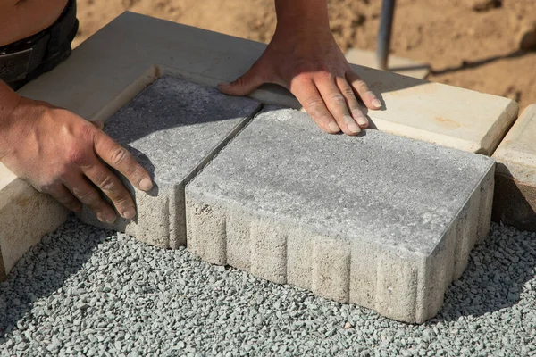 一个戴着手套的工匠把铺路石铺成层 在房子的四合院的沙质地基上铺灰色混凝土铺板 — 图库照片
