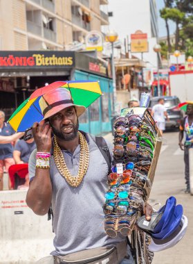 Palma de Mallorca, İspanya - 22 Haziran 2022: Siyahi adam Schinkenstrasse, İngiltere 'de güneş gözlüğü ve eğlenceli makaleler satıyor: Ballermann' da Ham Caddesi - engl: Palma 'da turistlere eğlenceli adam.