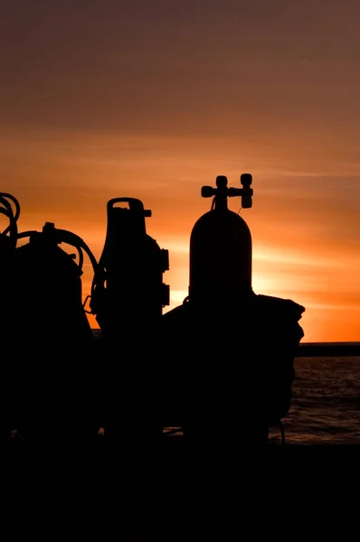 Scuba tanks sit against a boat rail during a beautiful sunset at sea.