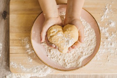 Children's hands with dough in the shape of a heart. Bake with love concept.