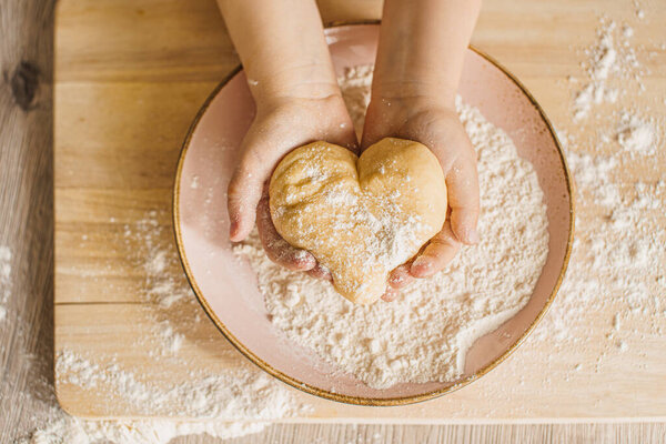 Children's hands with dough in the shape of a heart. Bake with love concept.