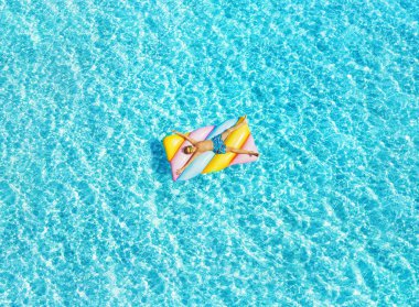 Havuzdaki şişme yatakta yatan çocuk. Otel havuzunda tatilde eğleniyorum. Renkli tatil kavramı.